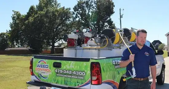 Weed Control NWA technician with spray wand beside branded lawn treatment truck